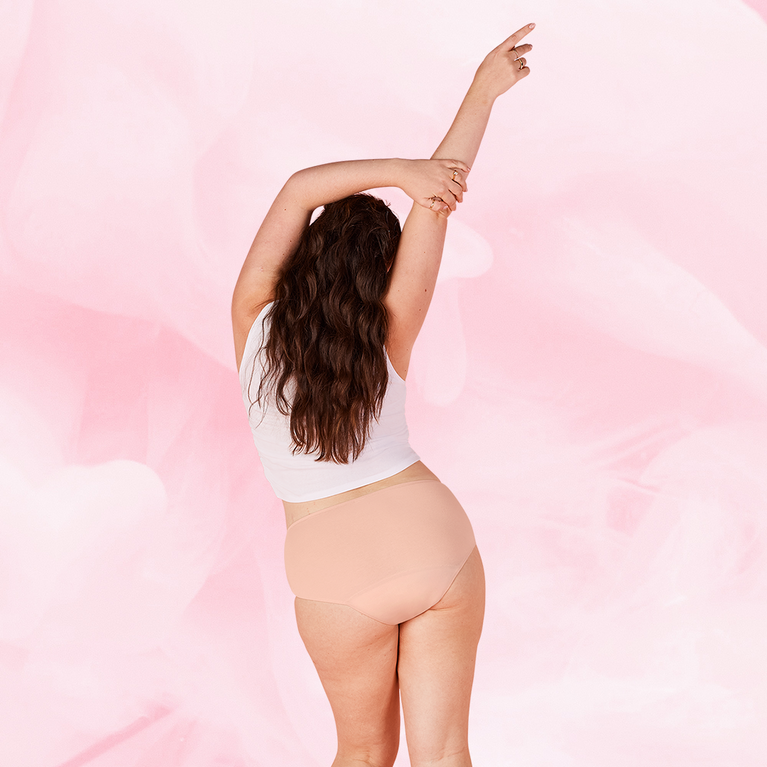 ComfortFit Essentials Hipster Heavy showcased by a woman pointing, wearing beige period pants, highlighting their fit and coverage designed for reliable, long-lasting period protection.
