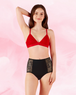 Against a soft pink backdrop, a person elegantly showcases intimawear by Bodyform™s AltText.ai - High Waist Floral Moderate. Wearing a red bralette with black high-waisted panties featuring lace panels, they smile warmly with one arm gracefully raised behind their head.